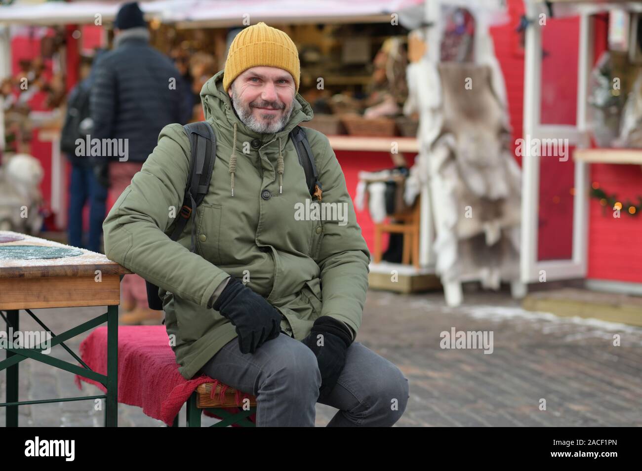Maturo uomo barbuto con zaino in appoggio al tavolo esterno sul mercato di Natale sulla piazza Kauppatori a Helsinki in Finlandia Foto Stock