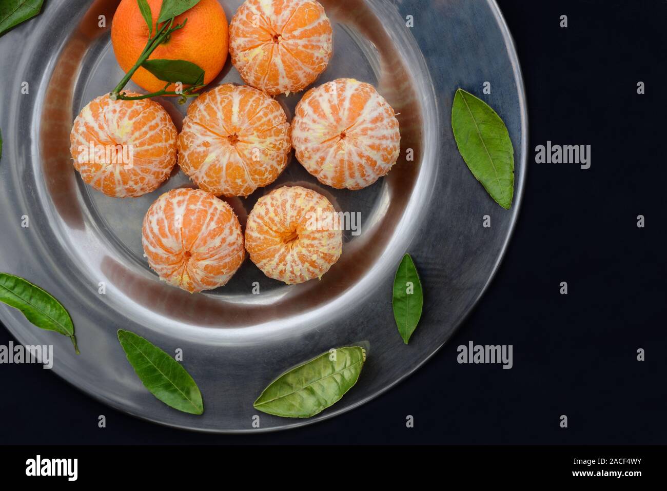 Freschi sbucciati tangerini con foglie verdi giacciono su una vecchia piastra di metallo contro uno sfondo scuro Foto Stock