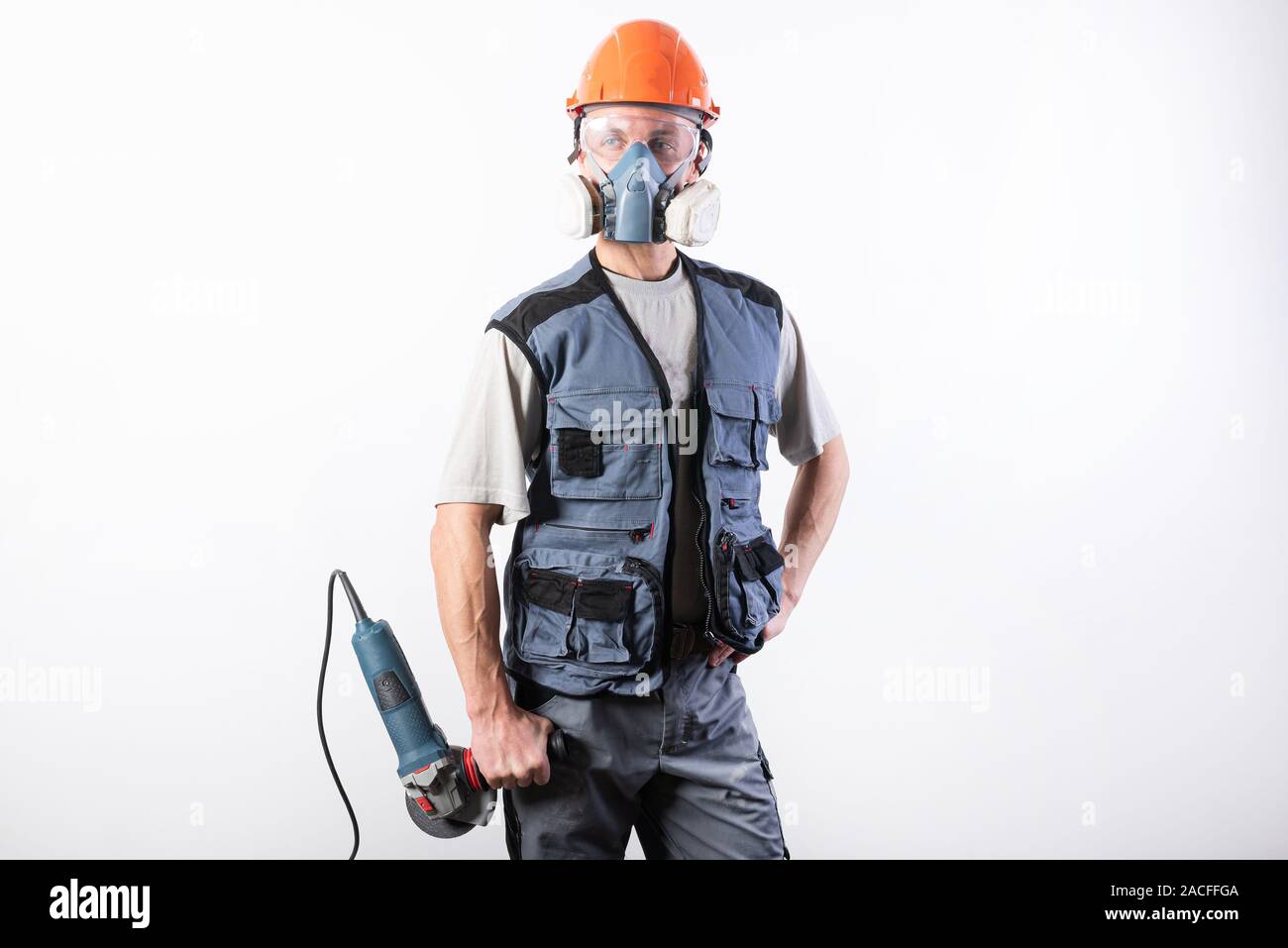 Builder in un casco e un respiratore, con una smerigliatrice angolare nelle sue mani. Foto Stock