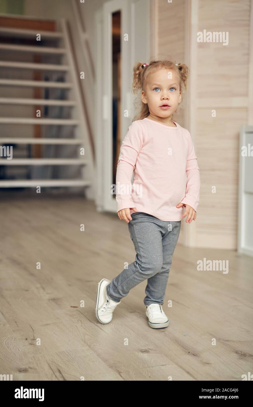 A piena lunghezza Ritratto di carino bambina indossa maglia rosa in posa di casa accogliente interno, spazio di copia Foto Stock