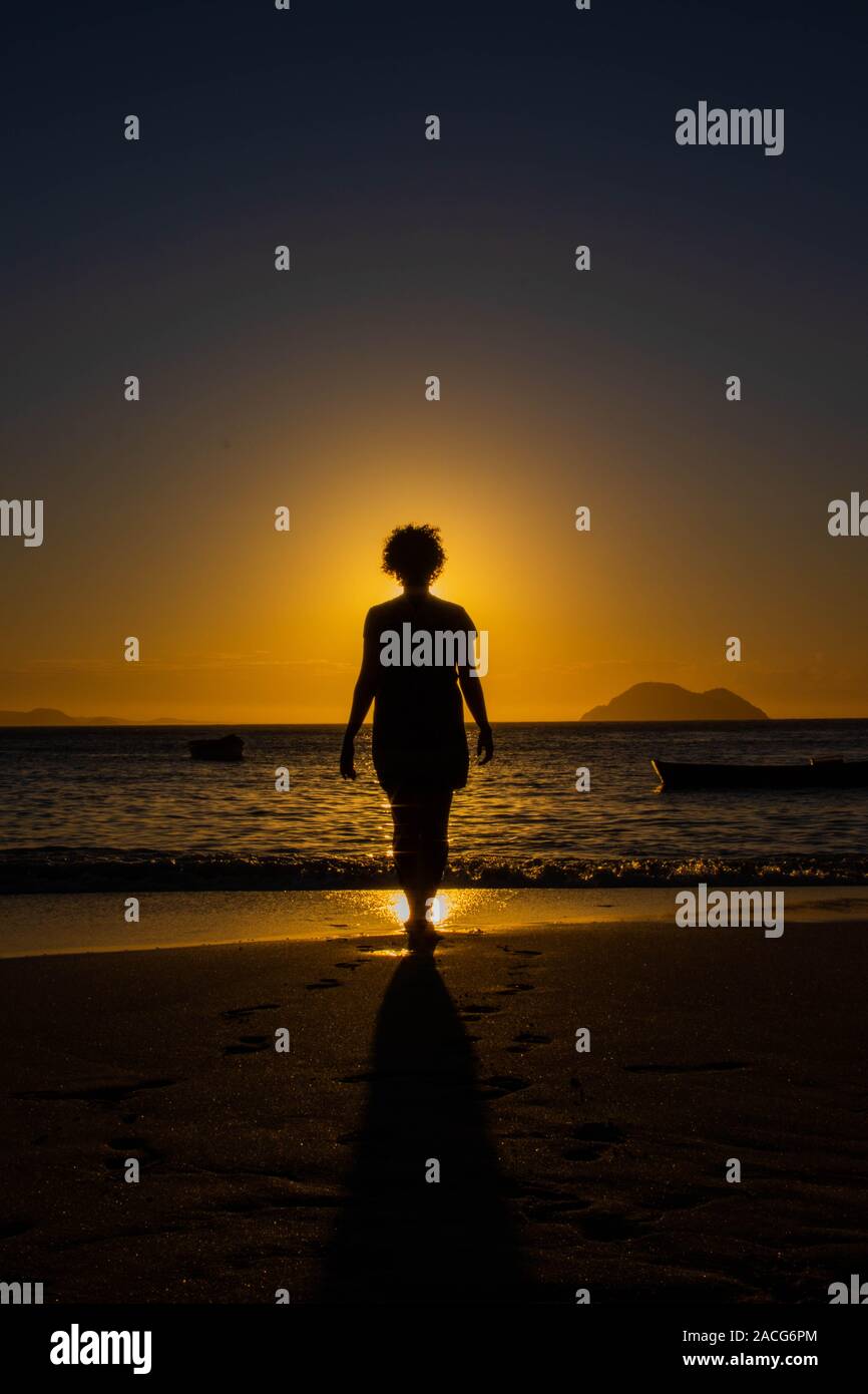 Silhouette di donna camminando sulla spiaggia al tramonto, Brasile Foto Stock