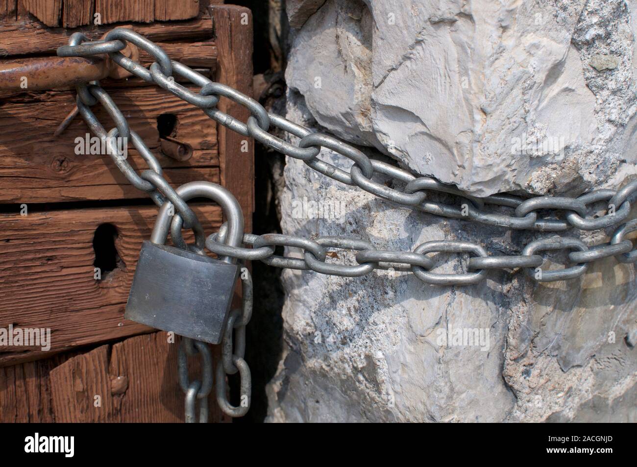 Chiudere l immagine di un lucchetto vicino con una robusta catena di metallo su una bella porta di legno su una vecchia casa in un villaggio nel nord Italia Foto Stock