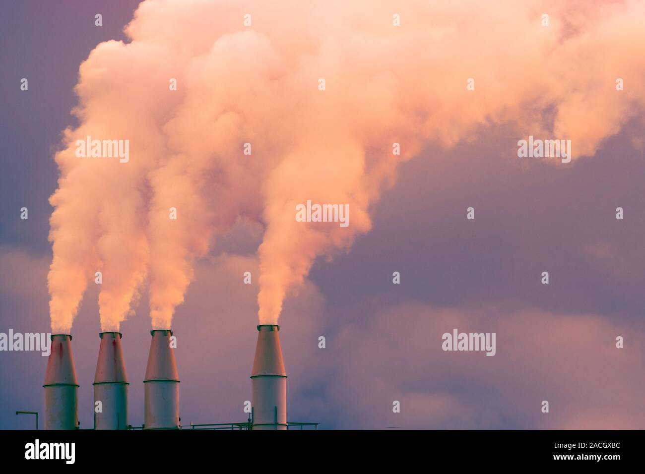 Fumo e vapore in salita l'aria dall'impianto di alimentazione di pile; nuvole scure sullo sfondo; concetto per inquinamento ambientale e il cambiamento climatico Foto Stock