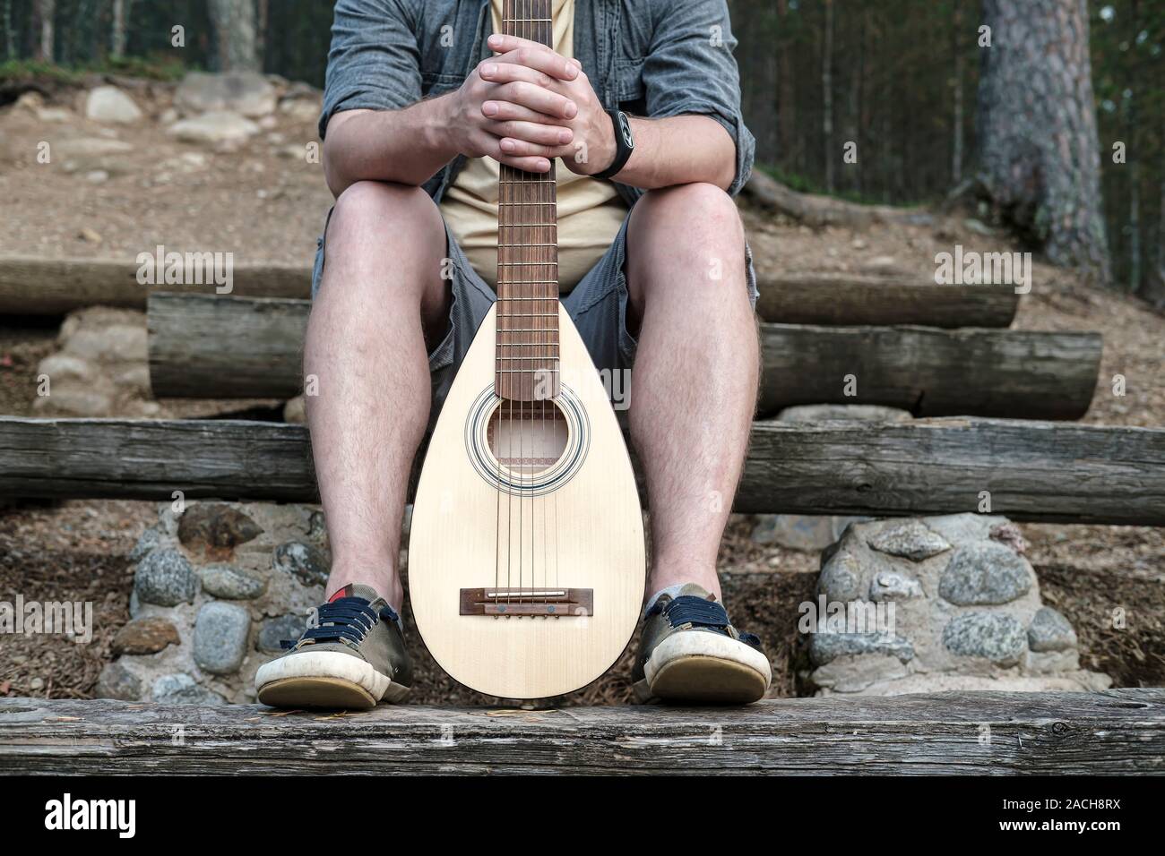 L'uomo detiene una chitarra acustica per il viaggio dietro un griff o collo, seduto su una panca in legno. Foto Stock