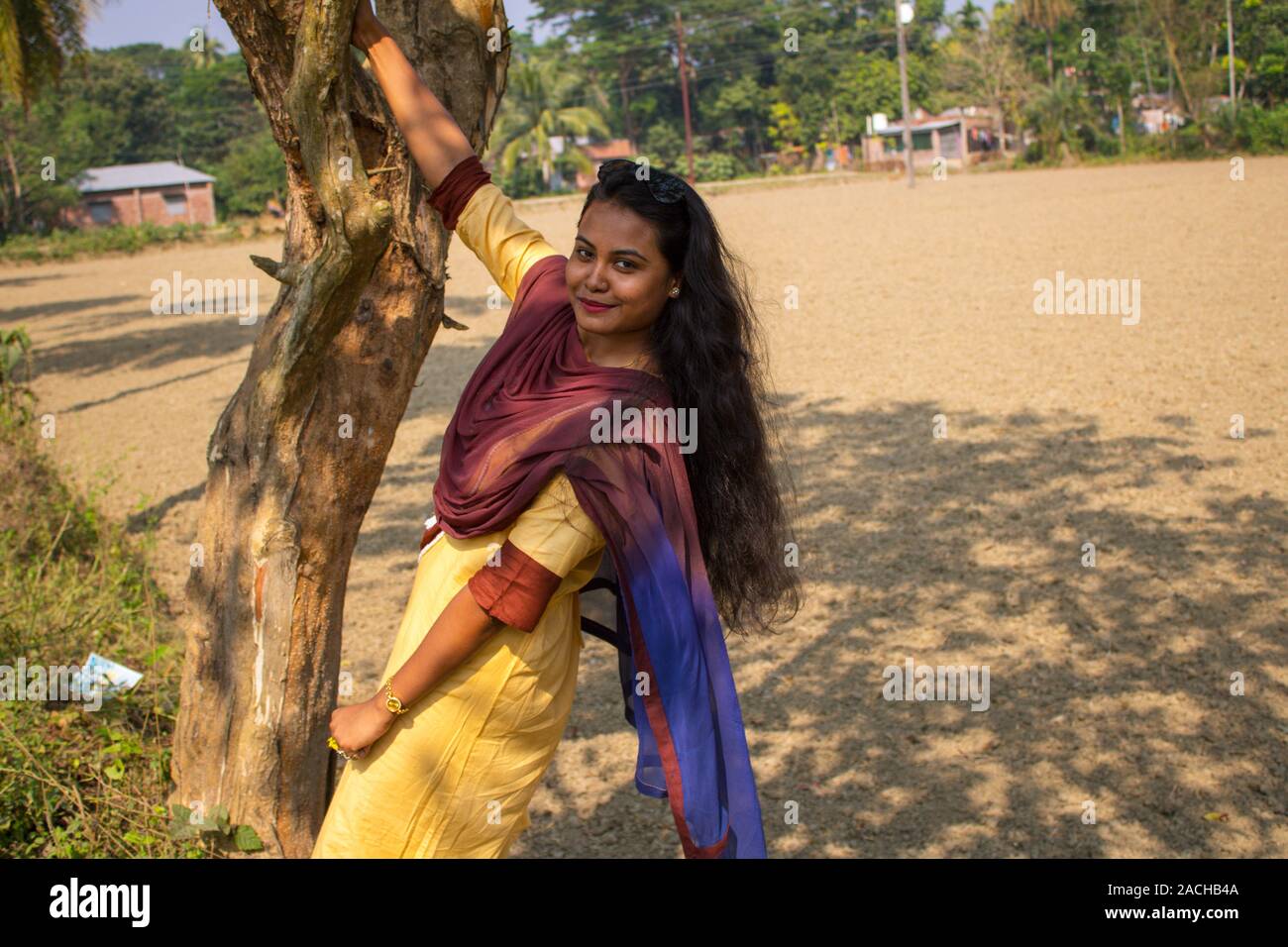 Ritratto di un carino,marrone,giocoso ragazza (bangladese o sud asiatico), nei pressi di un albero che ha lunghi capelli belli, lasciare vuoto il campo e gli alberi in background Foto Stock