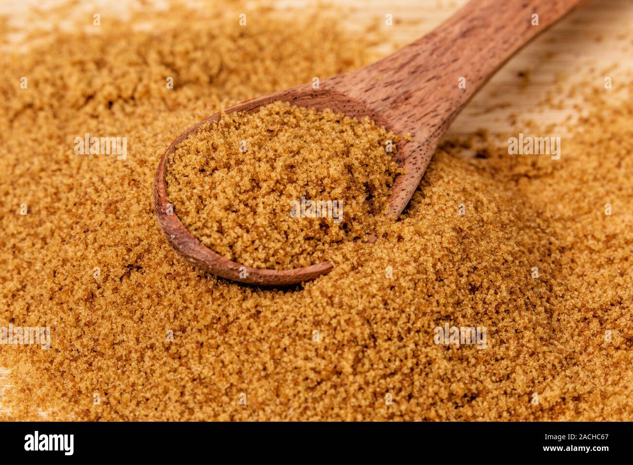 Cucchiaio di legno pieno di luce dolce di zucchero di canna su uno sfondo di legno Foto Stock