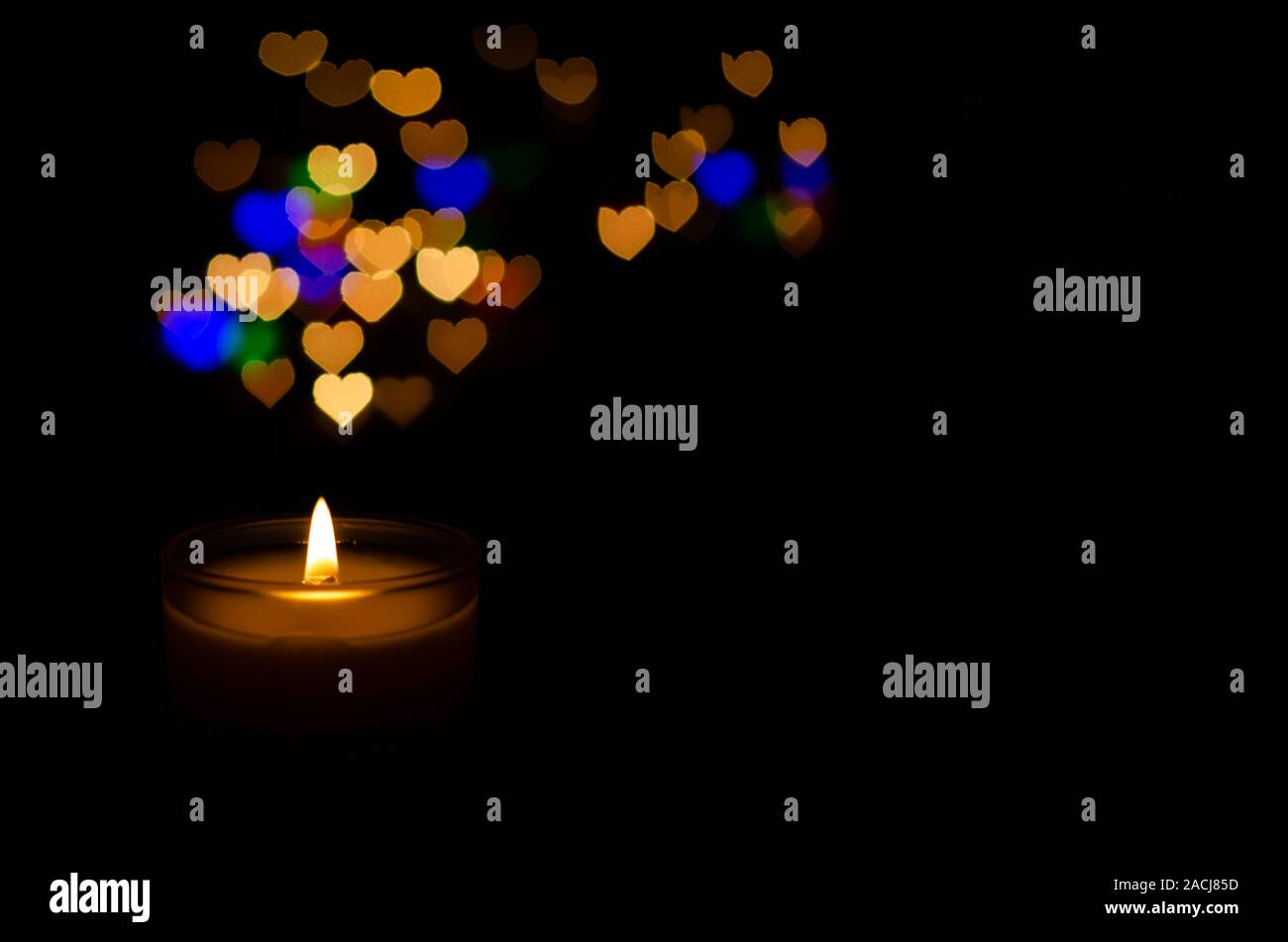 Bianco vetro aromatico candela con la fiamma e colorato amore bokeh di fondo di forma su sfondo scuro per il giorno di San Valentino. Foto Stock