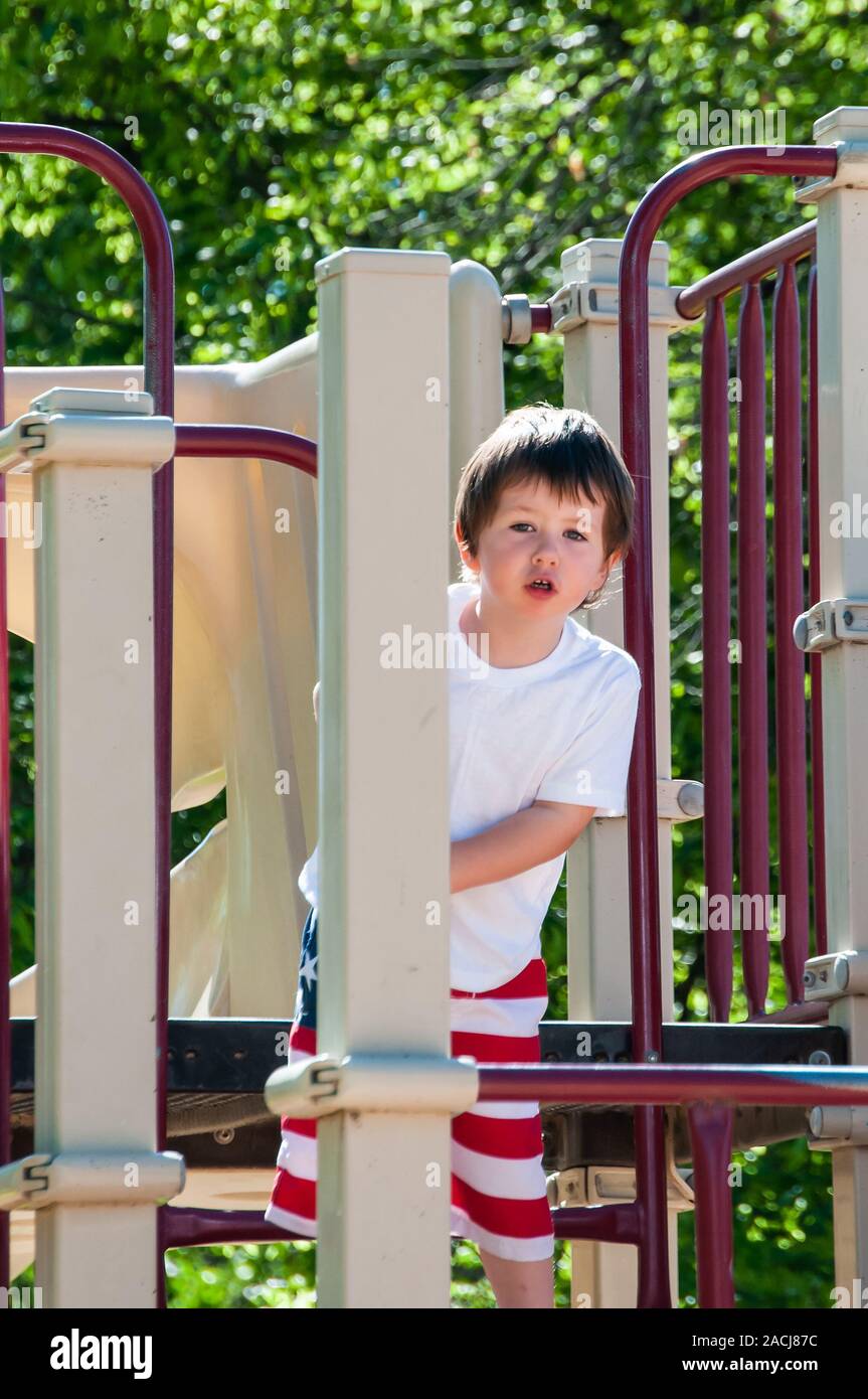 Little Boy giocando sul parco giochi presso il parco della città in una calda giornata estiva. Foto Stock