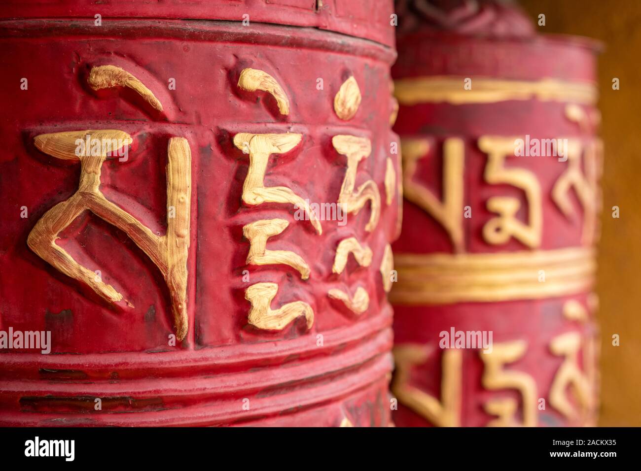 Rosso ruota di preghiera con il tibetano mantra Om mani padme hum all'ingresso del monastero locale Foto Stock