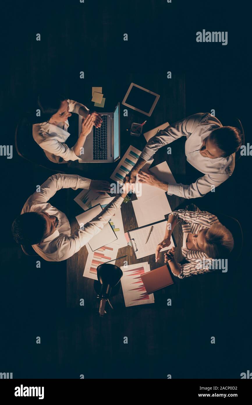 Angolo alto sopra visualizza foto verticale di quattro business partner seduta di lavoro del tavolo a tarda notte mani di scuotimento contratto firmato ovation colleghi Foto Stock