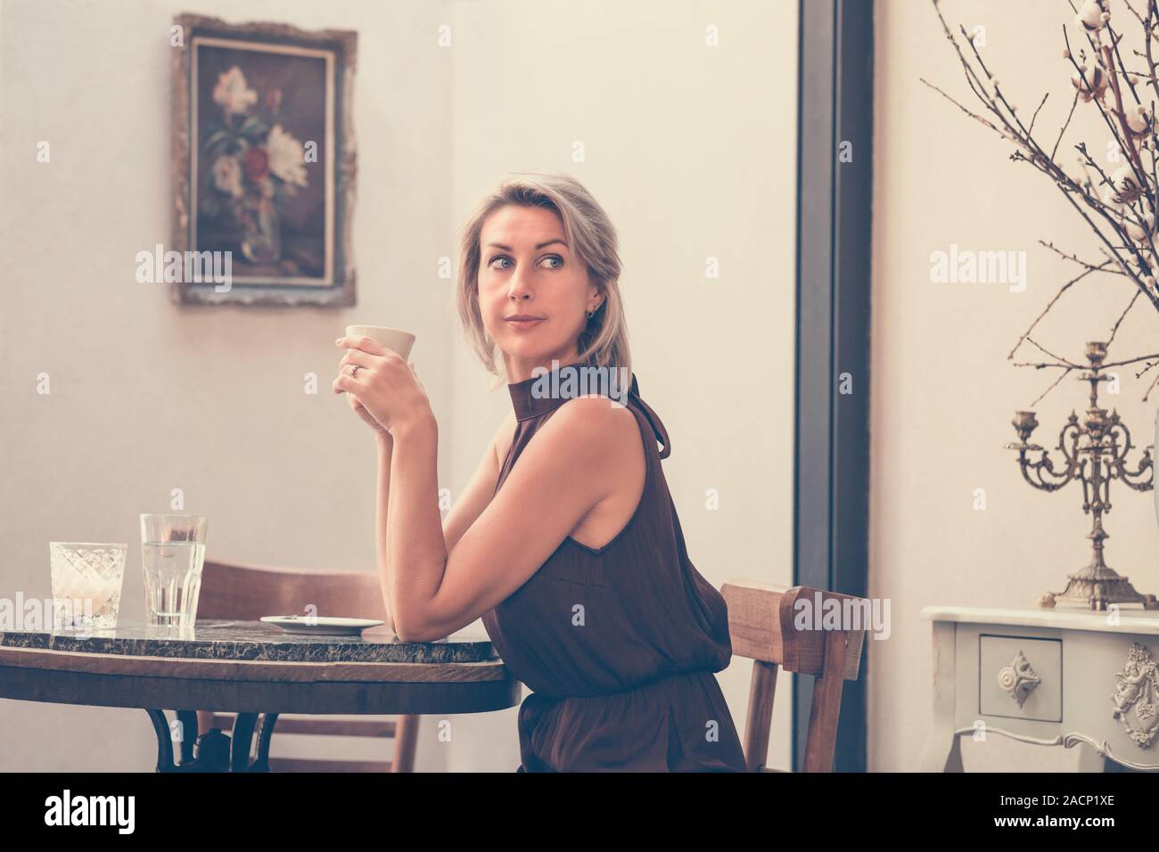 Tonica immagine della vista laterale della bella bionda signora seduta nel bar o un ristorante vicino alla finestra e di bere il caffè Foto Stock