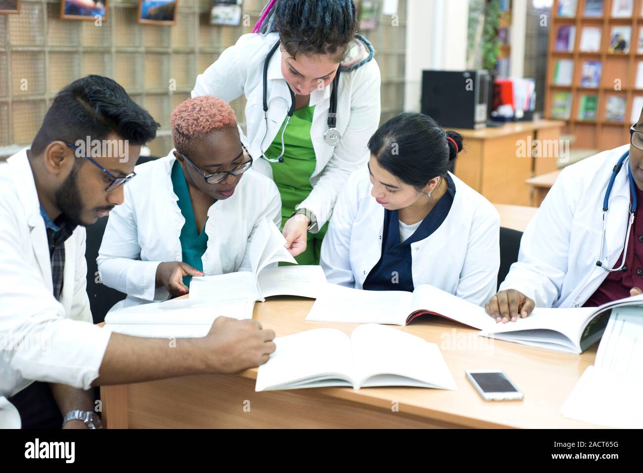 I giovani medici, razza mista. Essi siedono al tavolo, risolvere problemi medici. Le persone di sesso diverso, camici, abbigliamento medico, sono seduti ad un Foto Stock