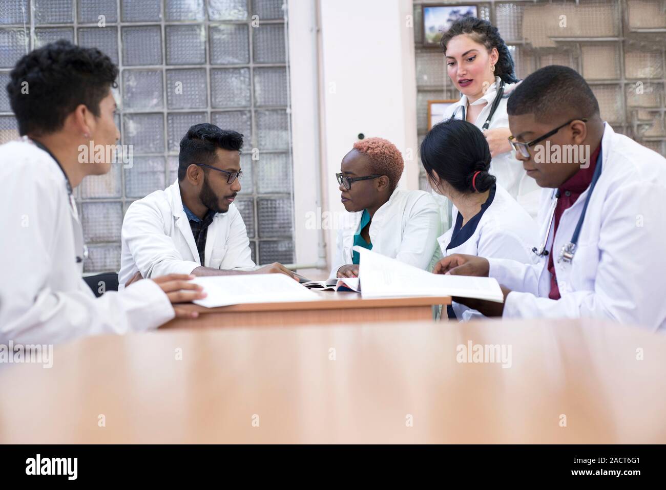I giovani medici, razza mista. Essi siedono al tavolo, risolvere problemi medici. Le persone di sesso diverso, camici, abbigliamento medico, sono seduti ad un Foto Stock