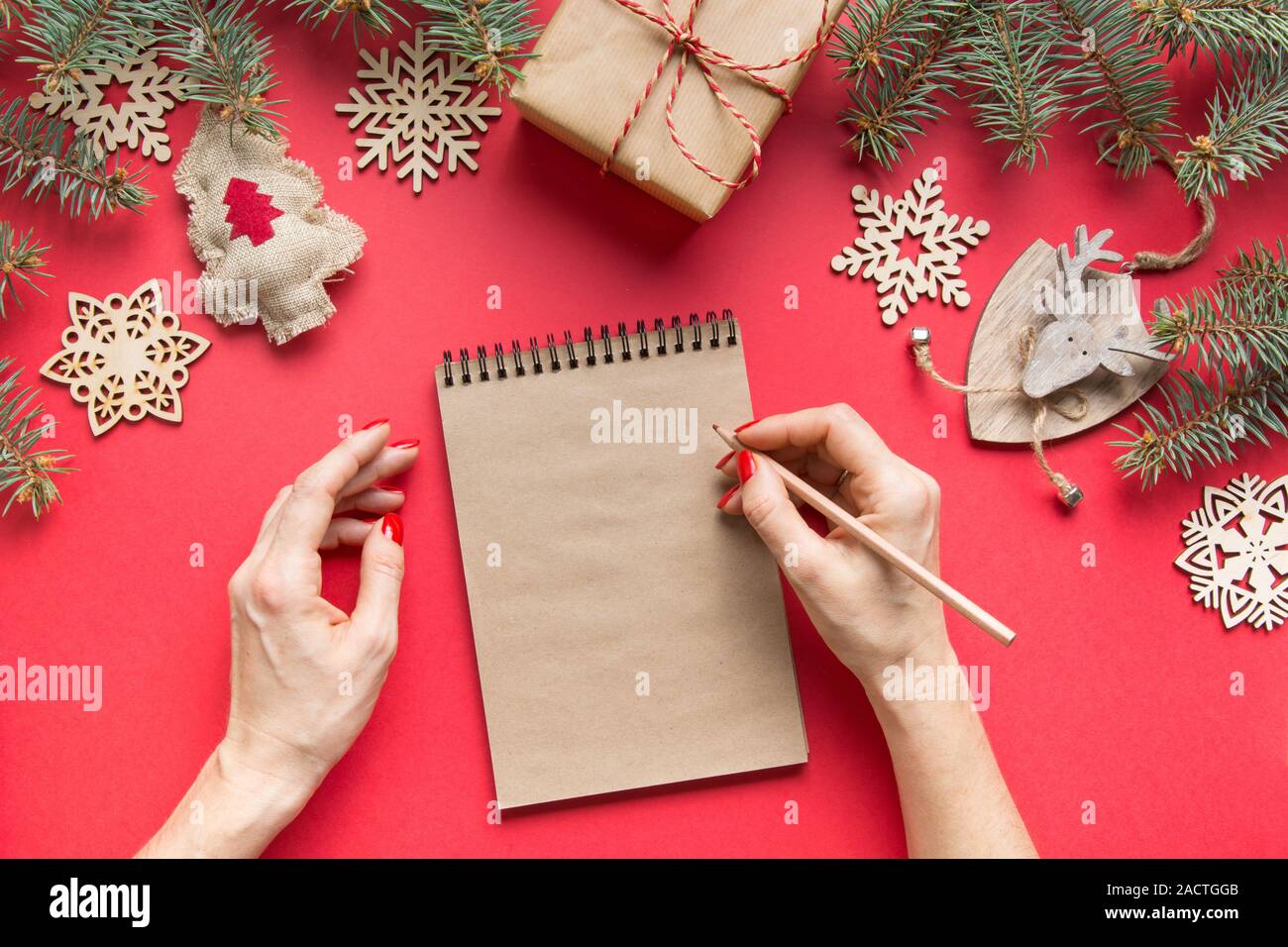 Zero rifiuti Nozione di Natale con legno arredamento naturale sul rosso. La donna la scrittura di invito. Obiettivi, checklist, piani, lista dei desideri, per fare la lista per il nuovo anno. Foto Stock