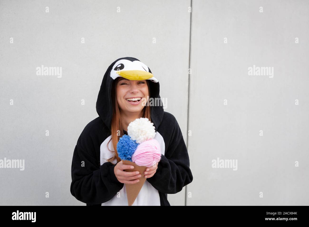 Bella e giovane donna in costume del pinguino è mangiare deco gelato nella parte anteriore della parete di cemento Foto Stock