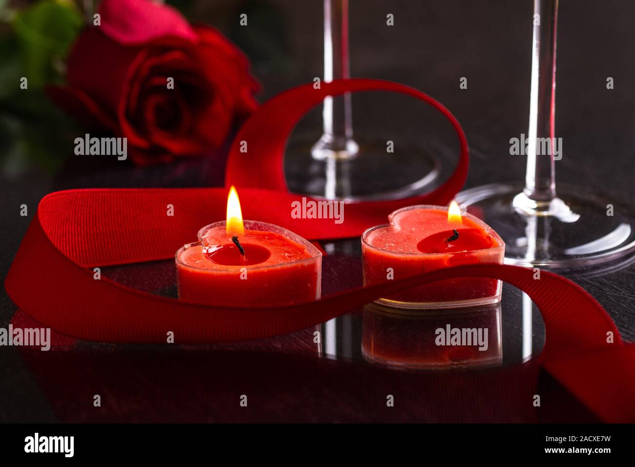 Primo piano di due cuore ardente di san Valentino a forma di candele con un nastro rosso e una rosa in background su un tavolo scuro Foto Stock