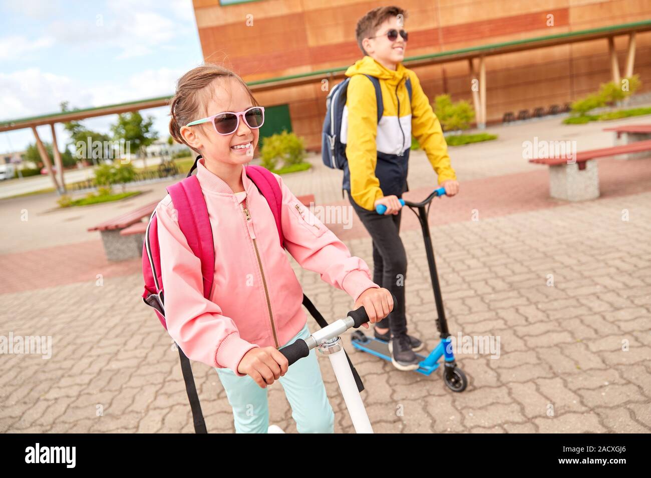 Istruzione, infanzia e concetto di persone - scuola di felici i bambini con zaini e scooter all'aperto Foto Stock