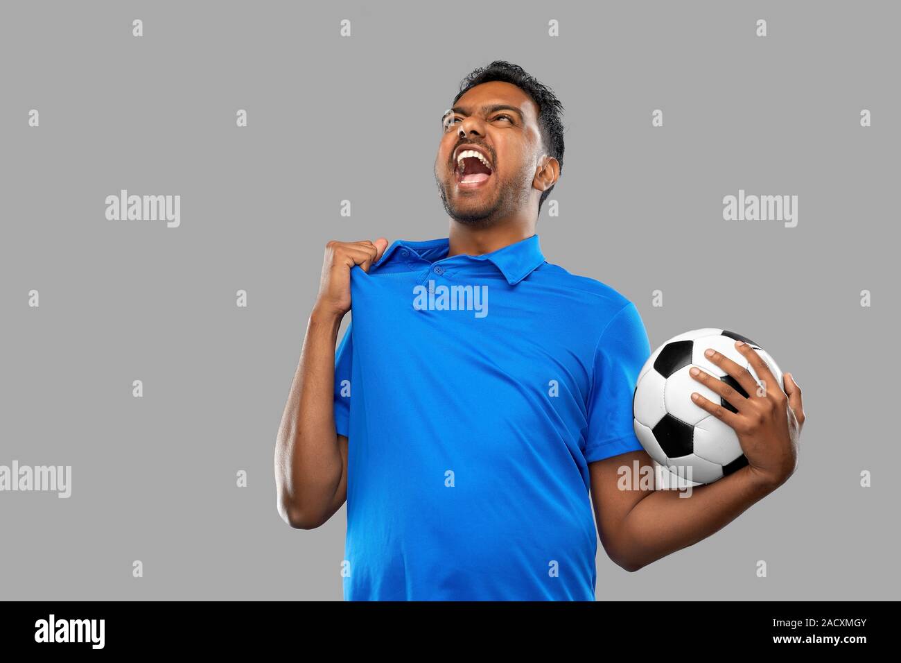 Sport e tempo libero giochi e concetto di successo - emotiva uomo indiano o tifoso di calcio con palla su sfondo grigio Foto Stock