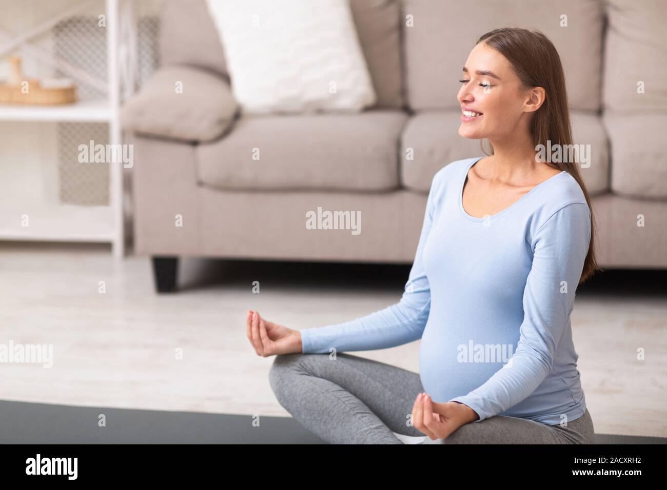 Donna incinta fare yoga seduta sul pavimento a casa Foto Stock