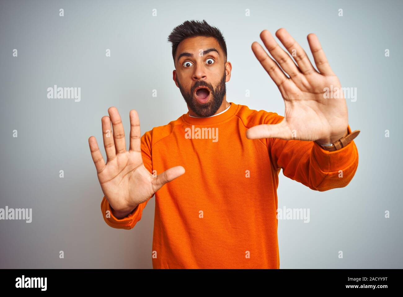 Giovani indiani uomo che indossa un maglione arancione isolato su sfondo  bianco di paura e terrore con la paura di espressione gesto di arresto con  le mani, gridando in Foto stock -