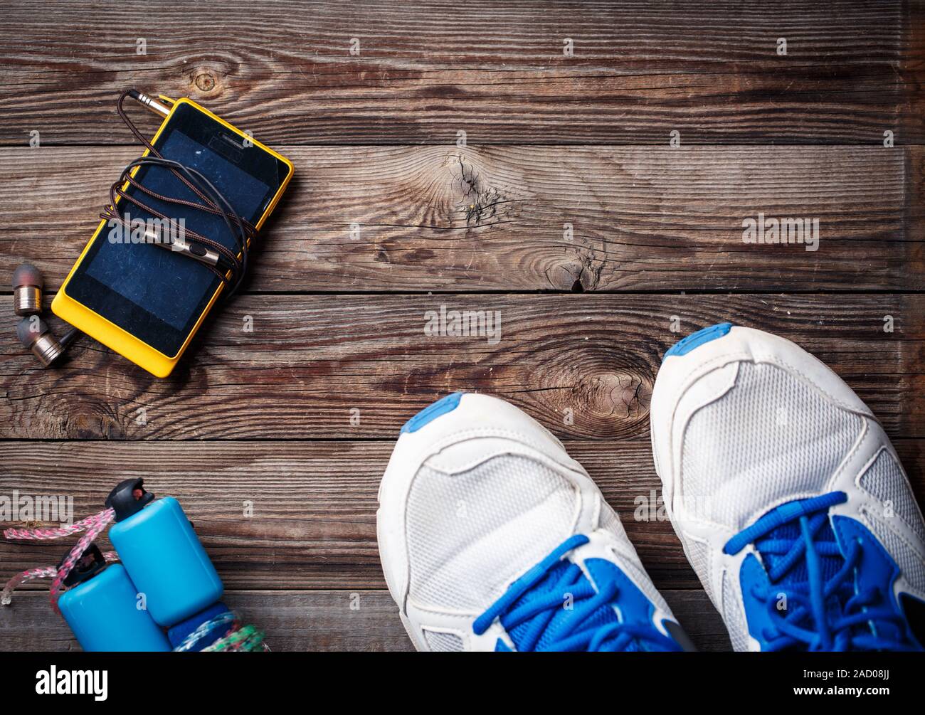Attrezzature sportive - scarpe da ginnastica, corda, smartphone e cuffie. Sport background sul pavimento di legno, vista dall'alto. Foto Stock