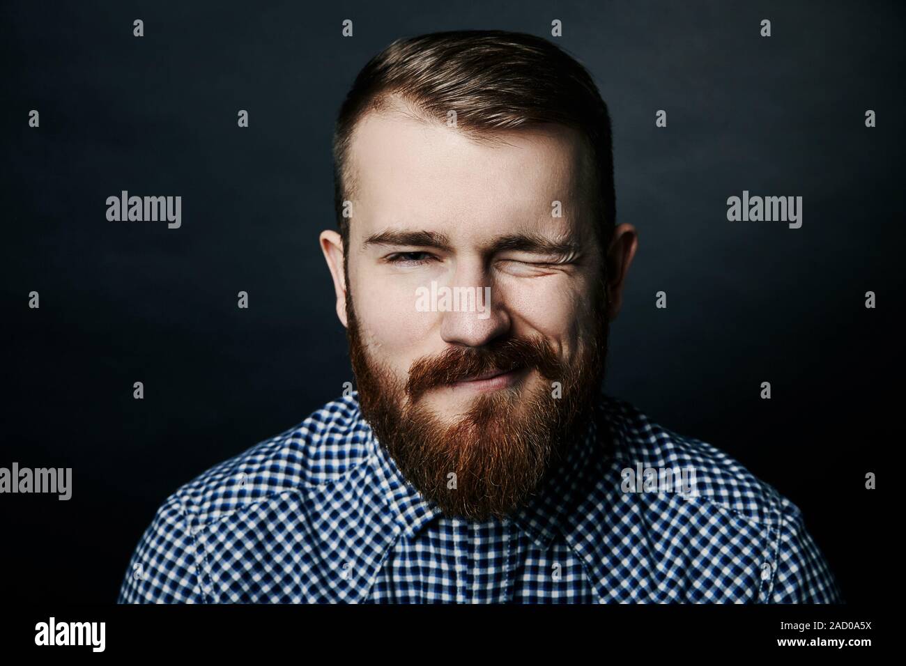 Winking rosso uomo barbuto ritratto in studio su sfondo scuro Foto Stock