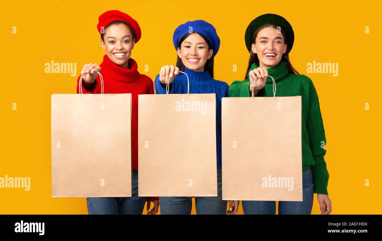 Le tre ragazze tenendo la carta Shopping Bags Standing, sfondo giallo, Mockup Foto Stock