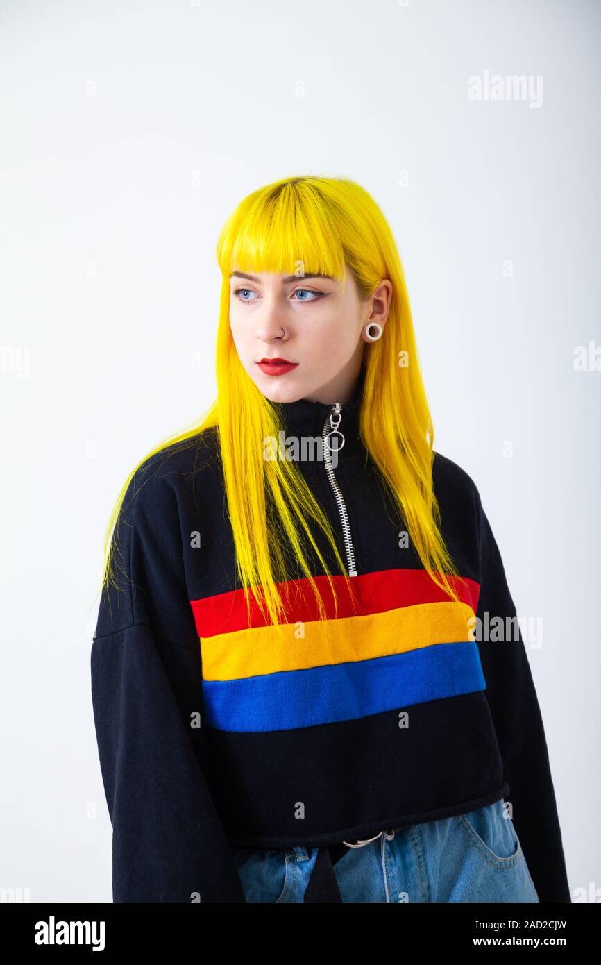 Una giovane donna con colore giallo brillante capelli indossando un colorato in cima contro uno sfondo bianco Foto Stock