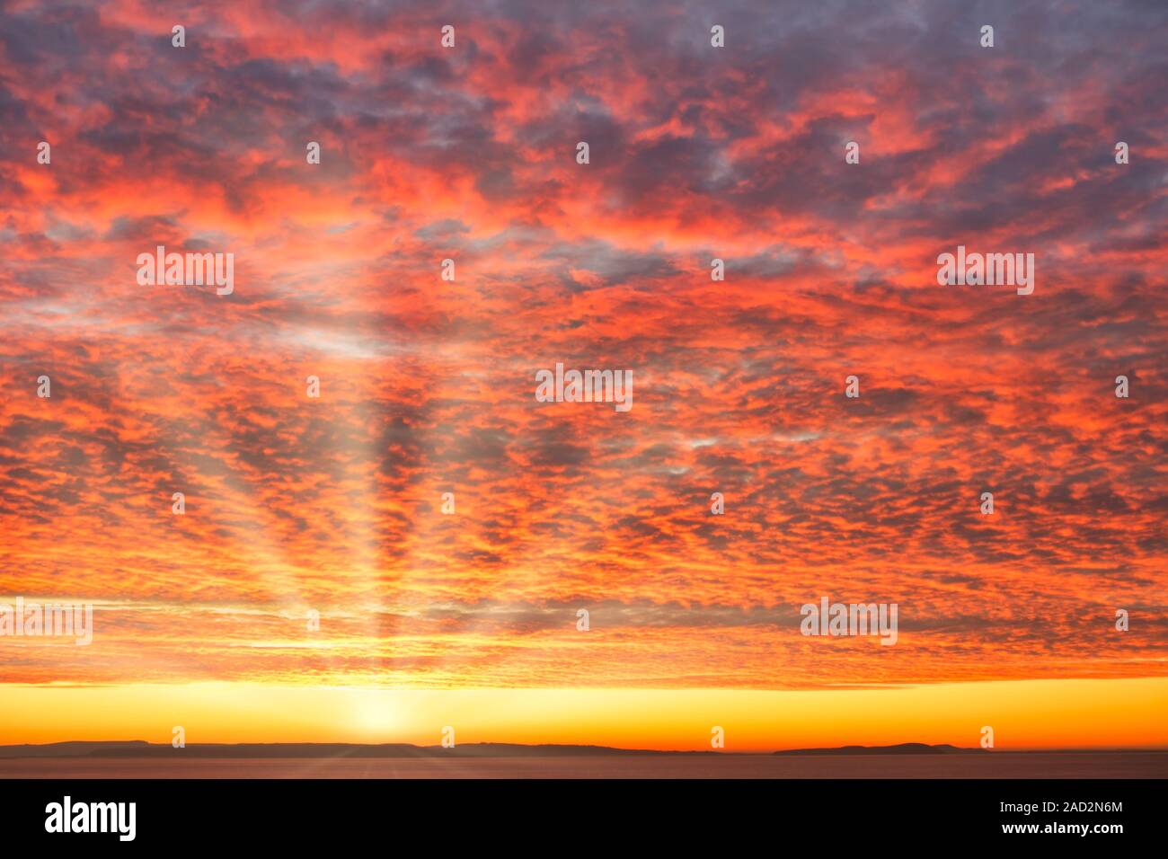 Fiery orange sunrise, il cielo al tramonto con drammatica sgombro formazione delle nuvole sopra il mare, sole e raggi solari. Foto Stock