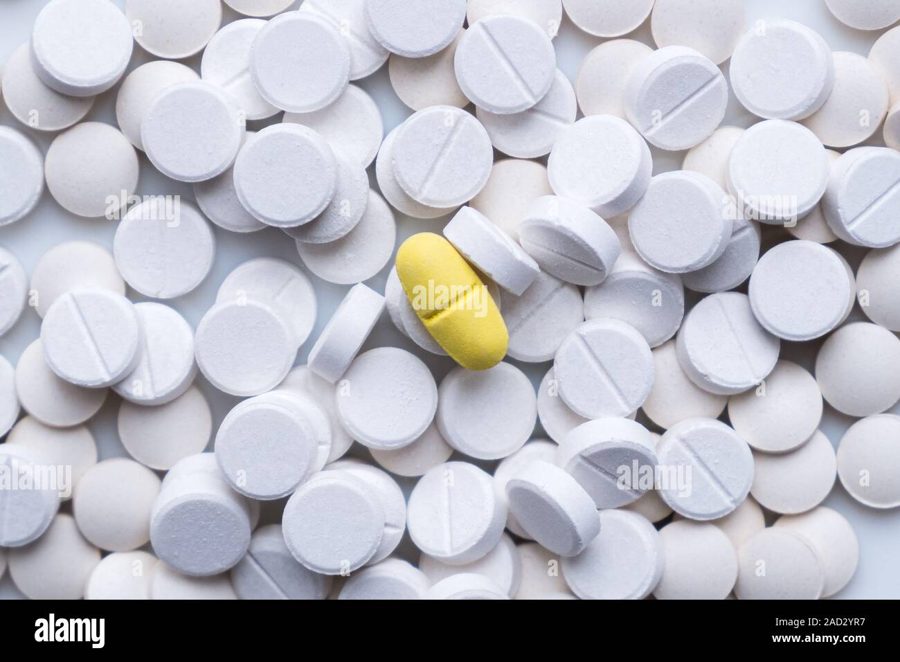 Pila di pillole di bianco e intorno a una gialla. Il concetto di diverse alternative o trattamento placebo Foto Stock