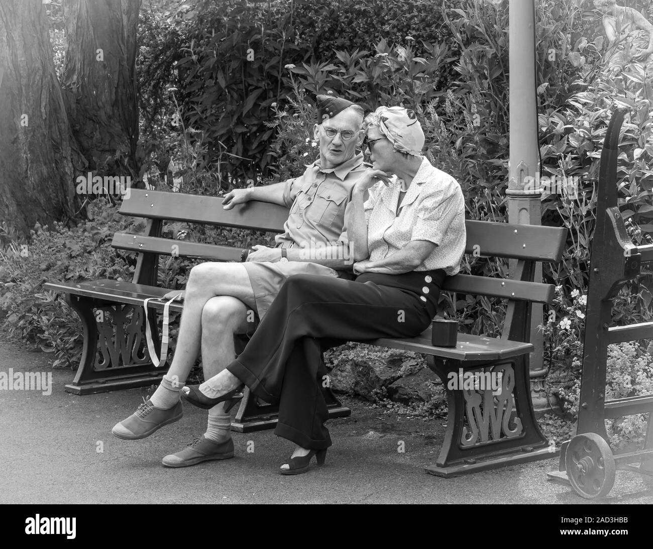 Fotografia in bianco e nero, coppia vintage (costume 1940s) seduta su panchina chattando alla stazione ferroviaria d'epoca sulla linea ferroviaria Severn Valley Heritage. Foto Stock