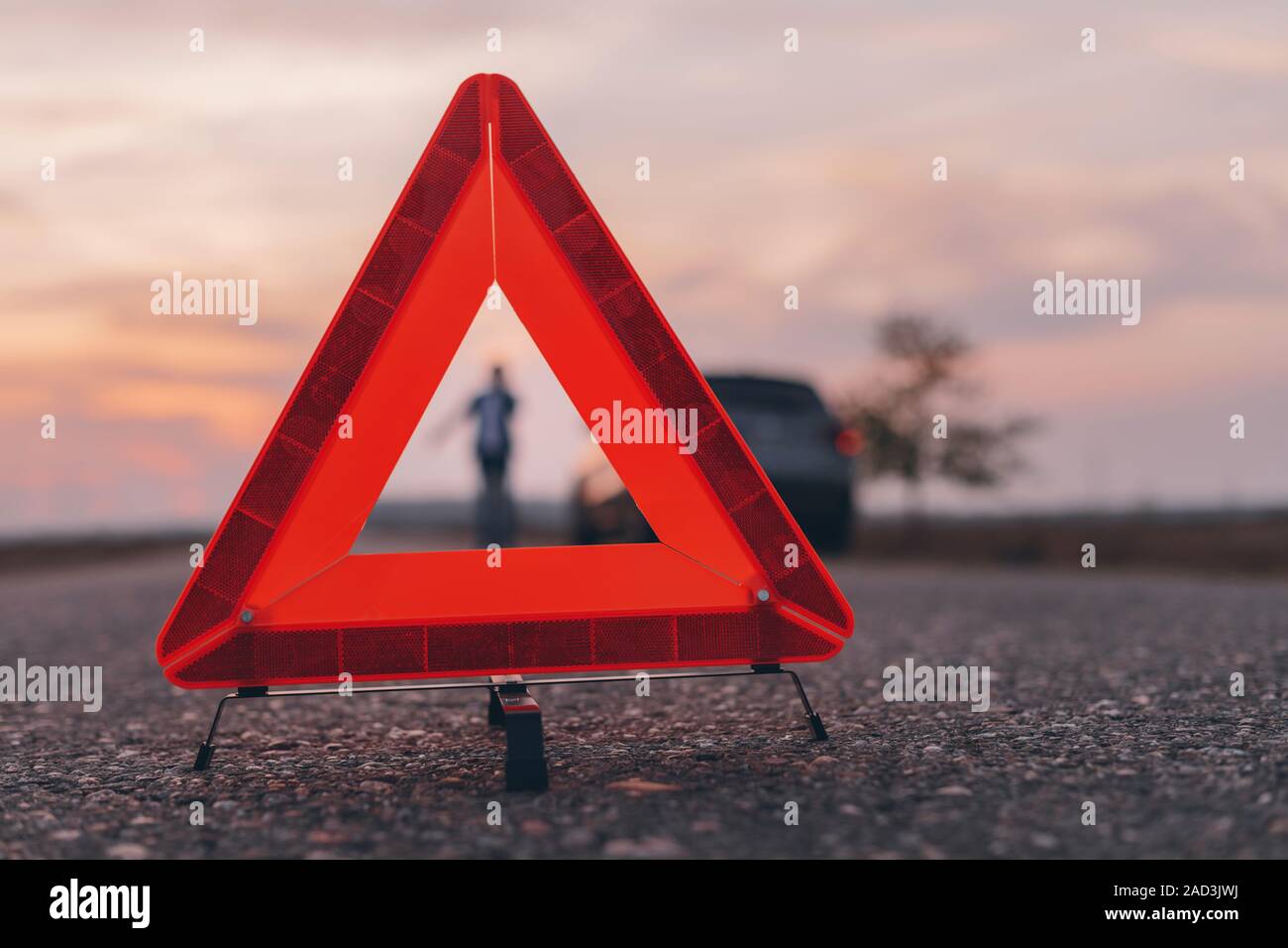 Il triangolo di avvertenza segno sulla strada, donna in blur sullo sfondo per chiedere assistenza stradale dalla Broken auto, il fuoco selettivo Foto Stock