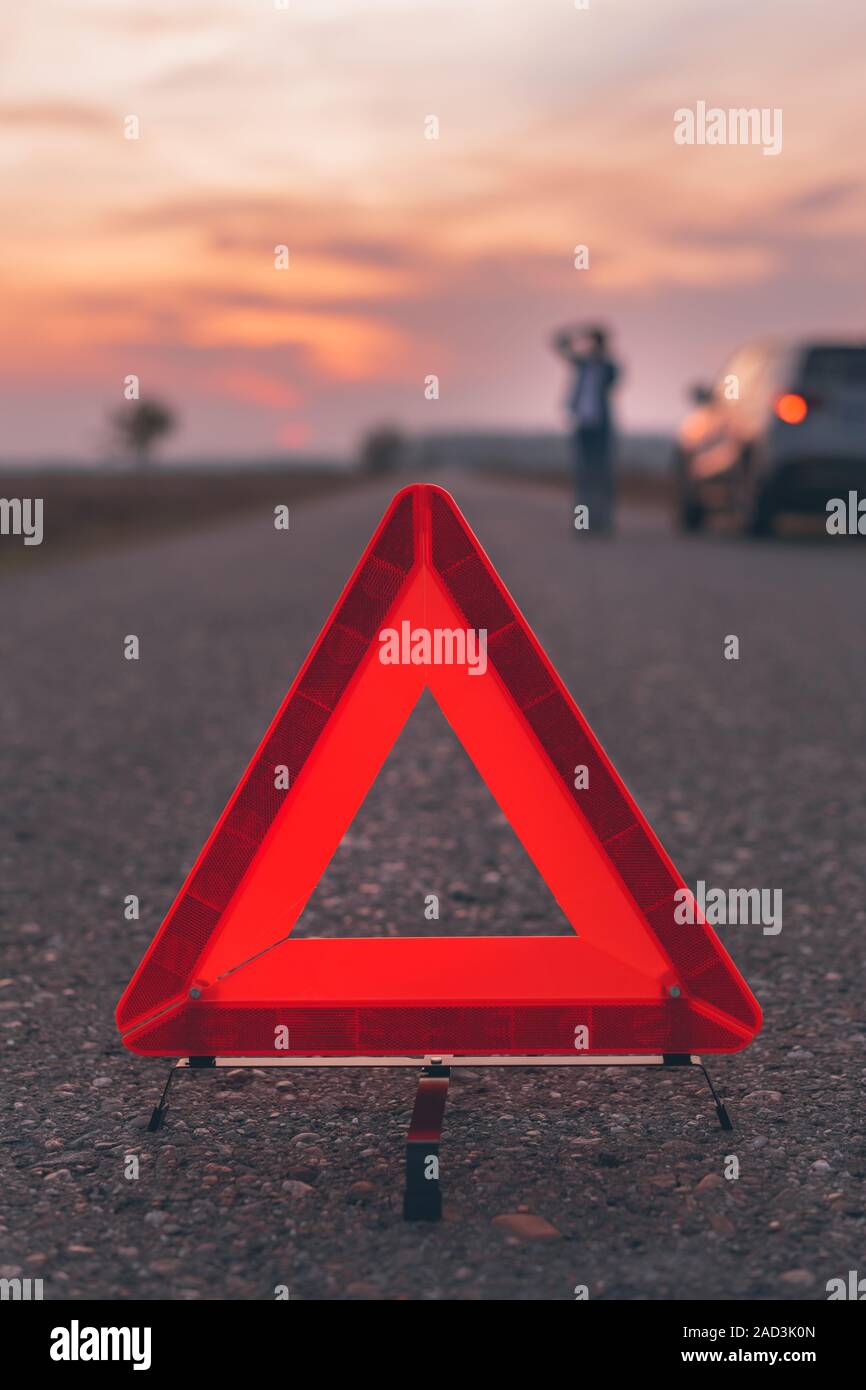 Il triangolo di avvertenza segno sulla strada, donna in blur sullo sfondo per chiedere assistenza stradale dalla Broken auto, il fuoco selettivo Foto Stock