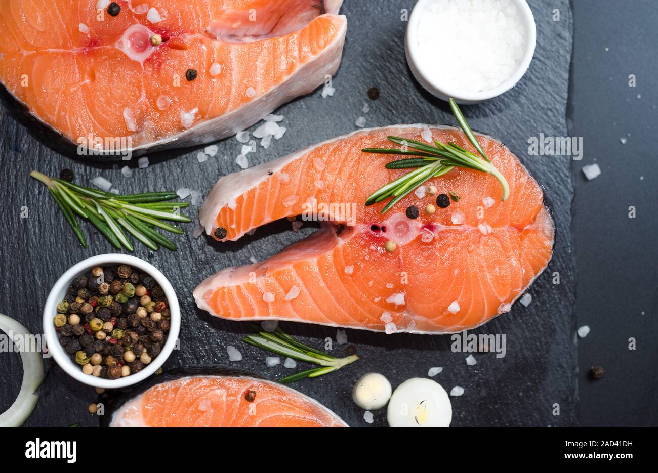 Raw bistecca di salmone al buio su un sfondo di pietra con cipolla, rosmarino, spezie, concetto dieta, grassi insaturi. Foto Stock