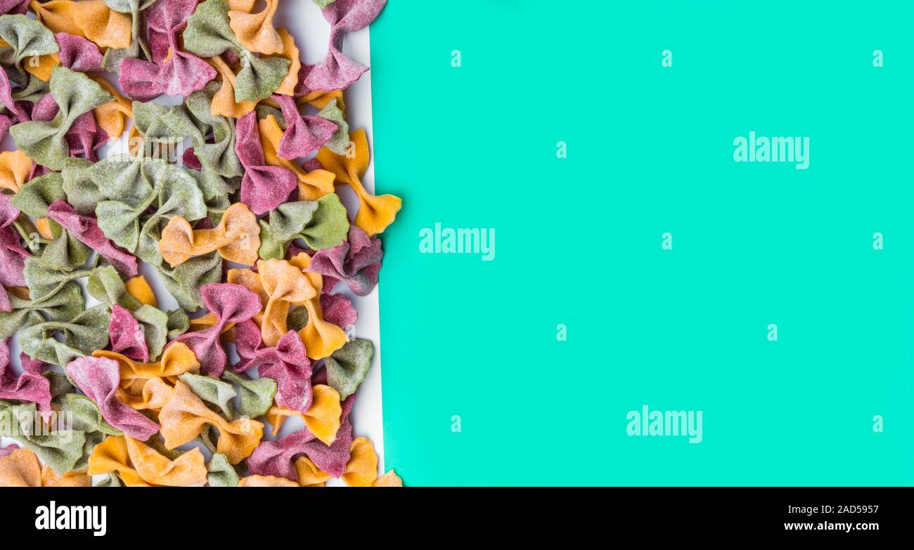 Pila di essiccato italiano Tricolore farfalle di pasta. Vari colori di bow tie su moda verde menta colore di sfondo Foto Stock