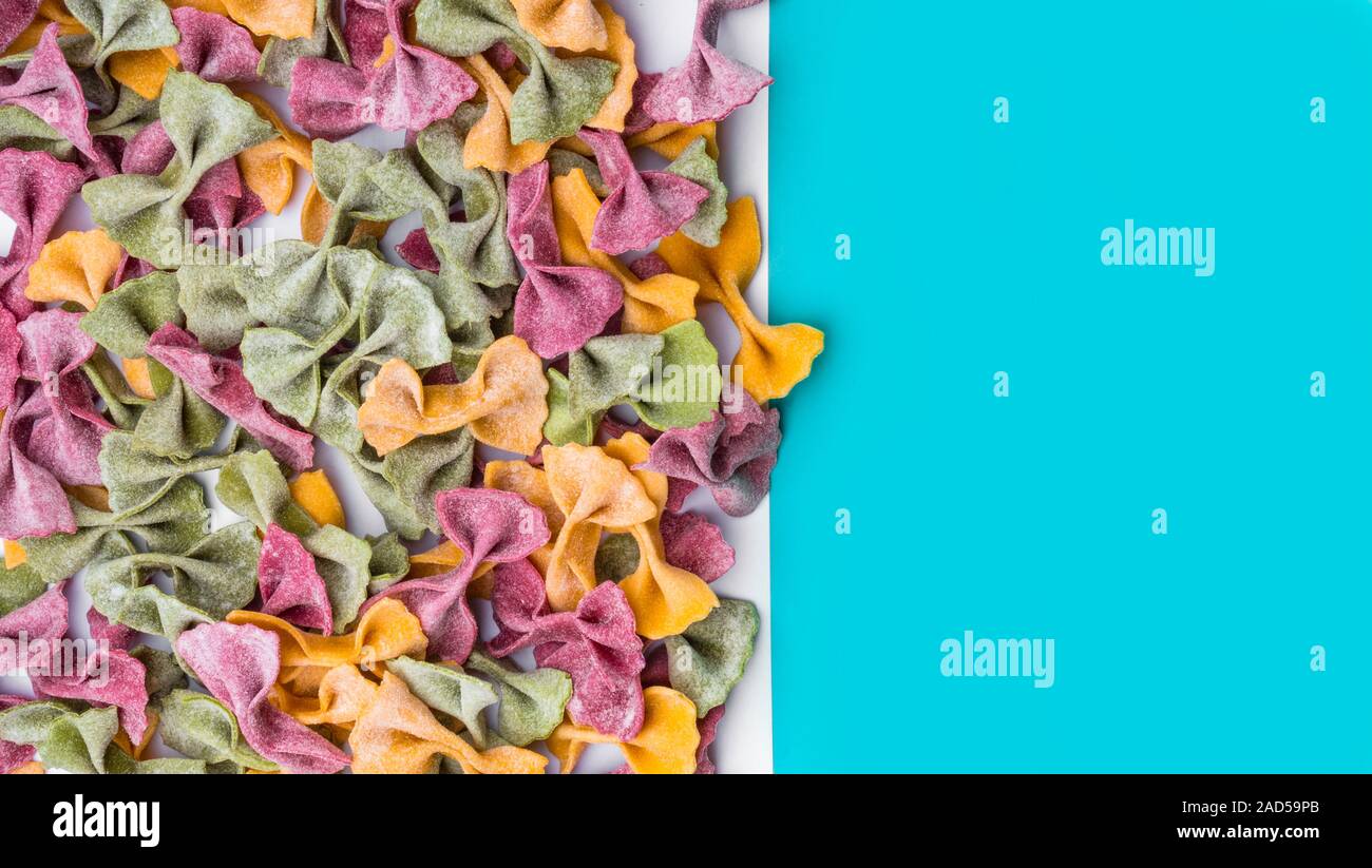 Pila di essiccato italiano Tricolore farfalle di pasta. Vari colori di bow tie blu su sfondo colorato Foto Stock