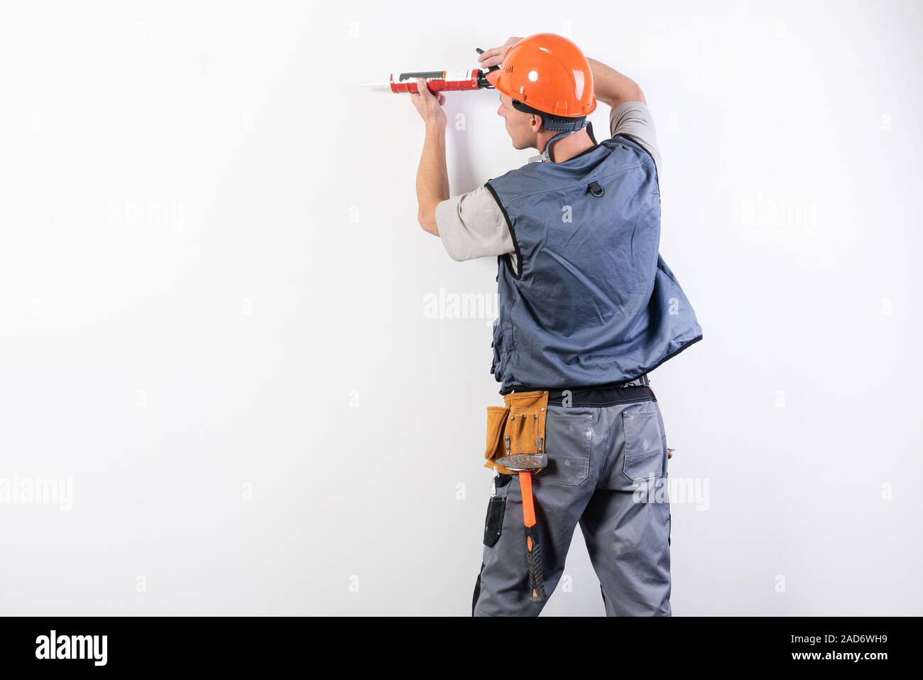 Un builder in un casco con silicone in una pistola di montaggio, mira al telaio. Foto Stock