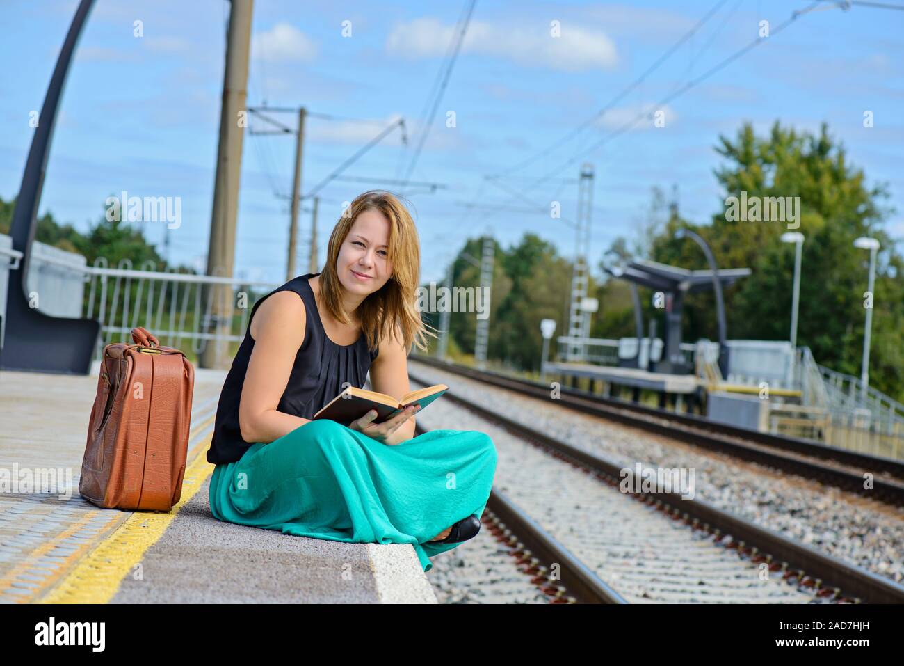 Giovane donna attraente in gonna lunga seduta su La stazione ferroviaria e la lettura di un libro Foto Stock