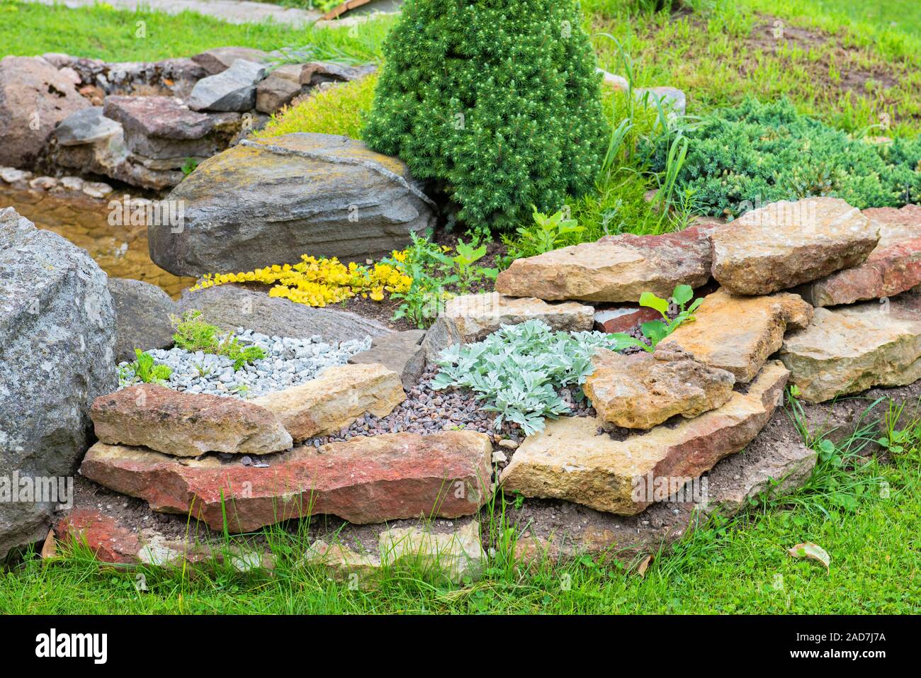 Giardino alpino con un ponte e un piccolo stagno con acqua Foto Stock