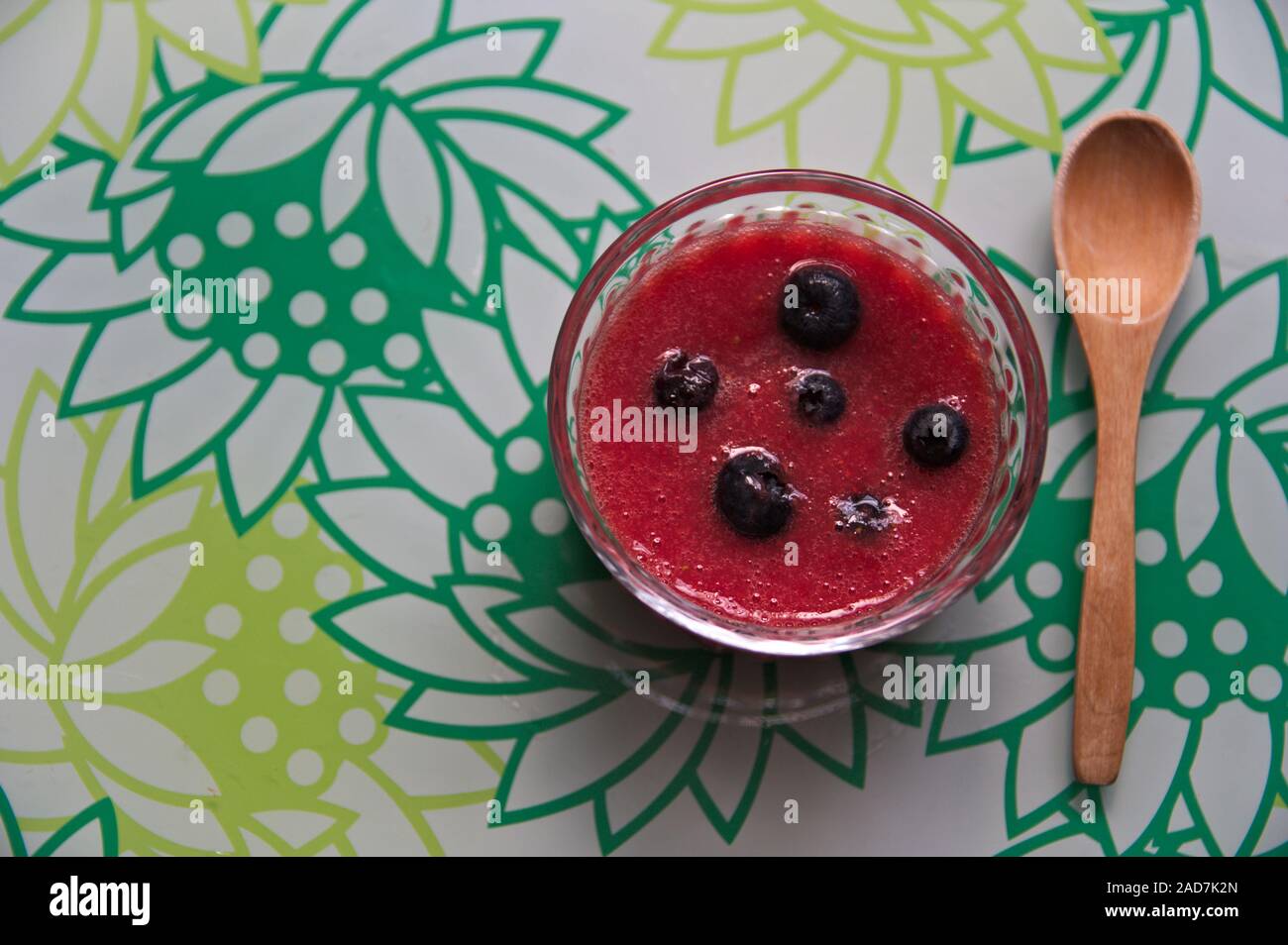 Piatto di laici una superficie decorata su cui possiamo vedere una ciotola con il succo di fragole con mirtilli e un cucchiaio di legno e lo spazio sulla sinistra Foto Stock