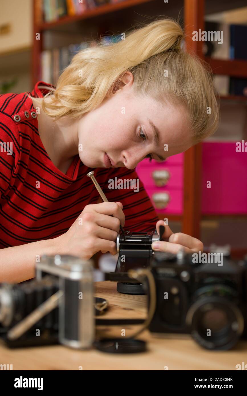 Tall shot di una ragazza adolescente servendosi di un piccolo cacciavite per riparare un antico fotocamera a pellicola. Altre telecamere sono al di fuori della messa a fuoco in primo piano. Foto Stock