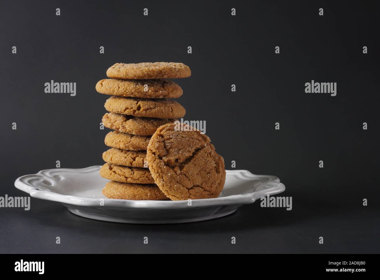 Una pila di fragranti biscotti allo zenzero su una piastra bianca e uno sfondo nero; spazio di copia Foto Stock
