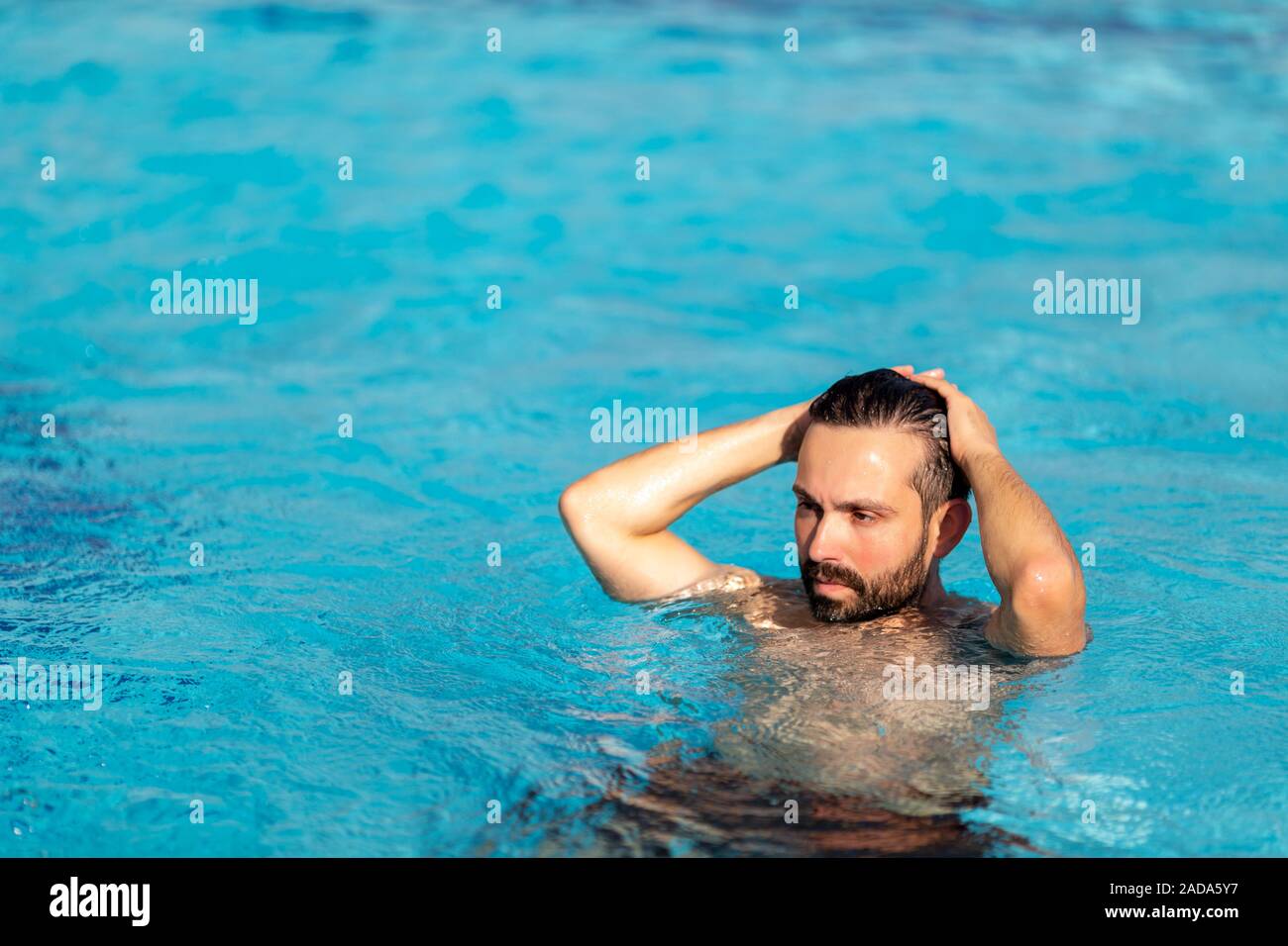 L uomo è nuotare nella piscina con spray sulla faccia con un effetto drammatico. Il resto, concetto di viaggio. Foto Stock
