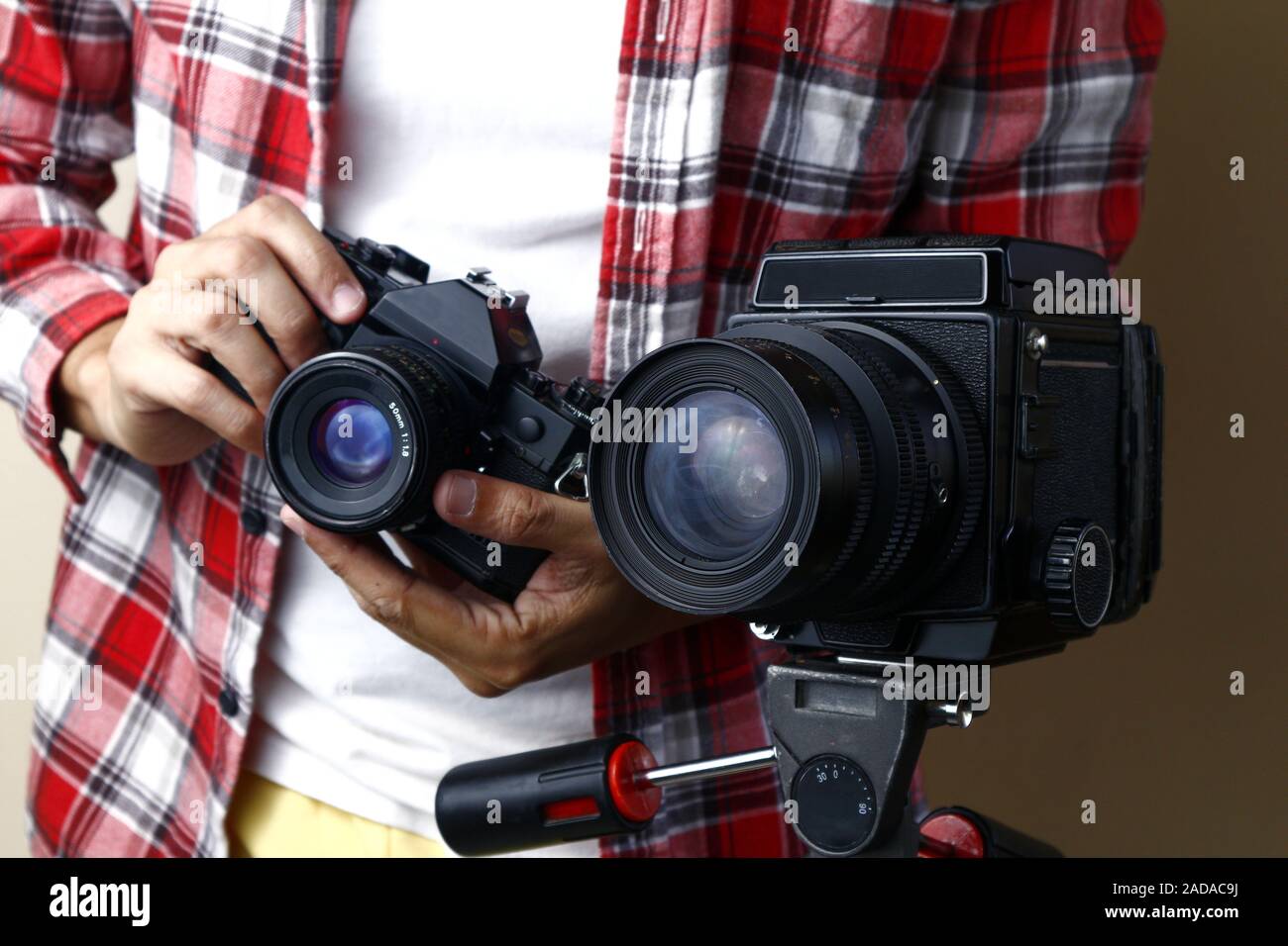 Foto di un uomo con una pellicola di 35mm Fotocamera e in piedi dietro un medio formato fotocamera a pellicola su un treppiede Foto Stock