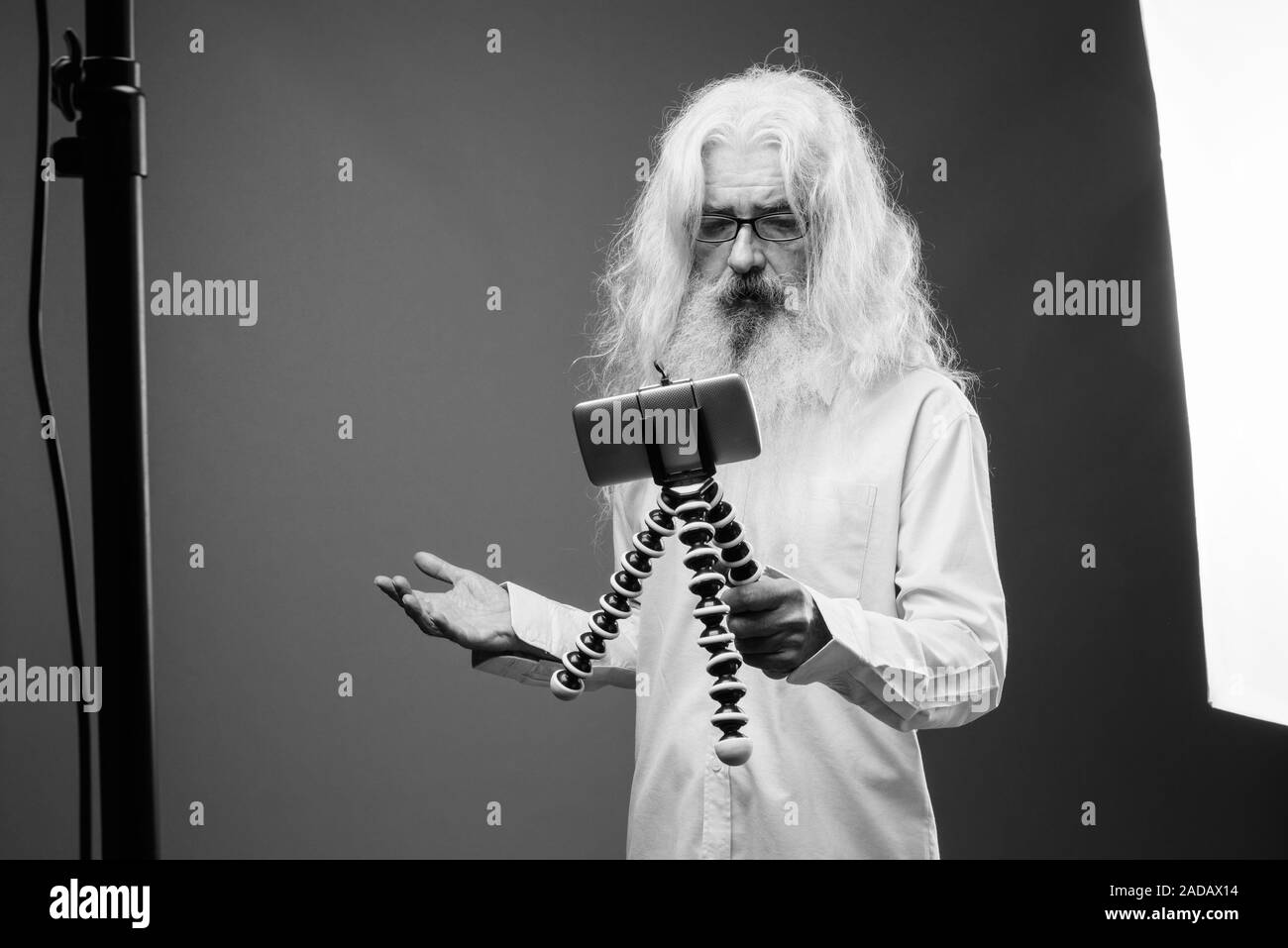 Senior uomo con i capelli lunghi e la barba vlogging con telefono in bianco e nero Foto Stock