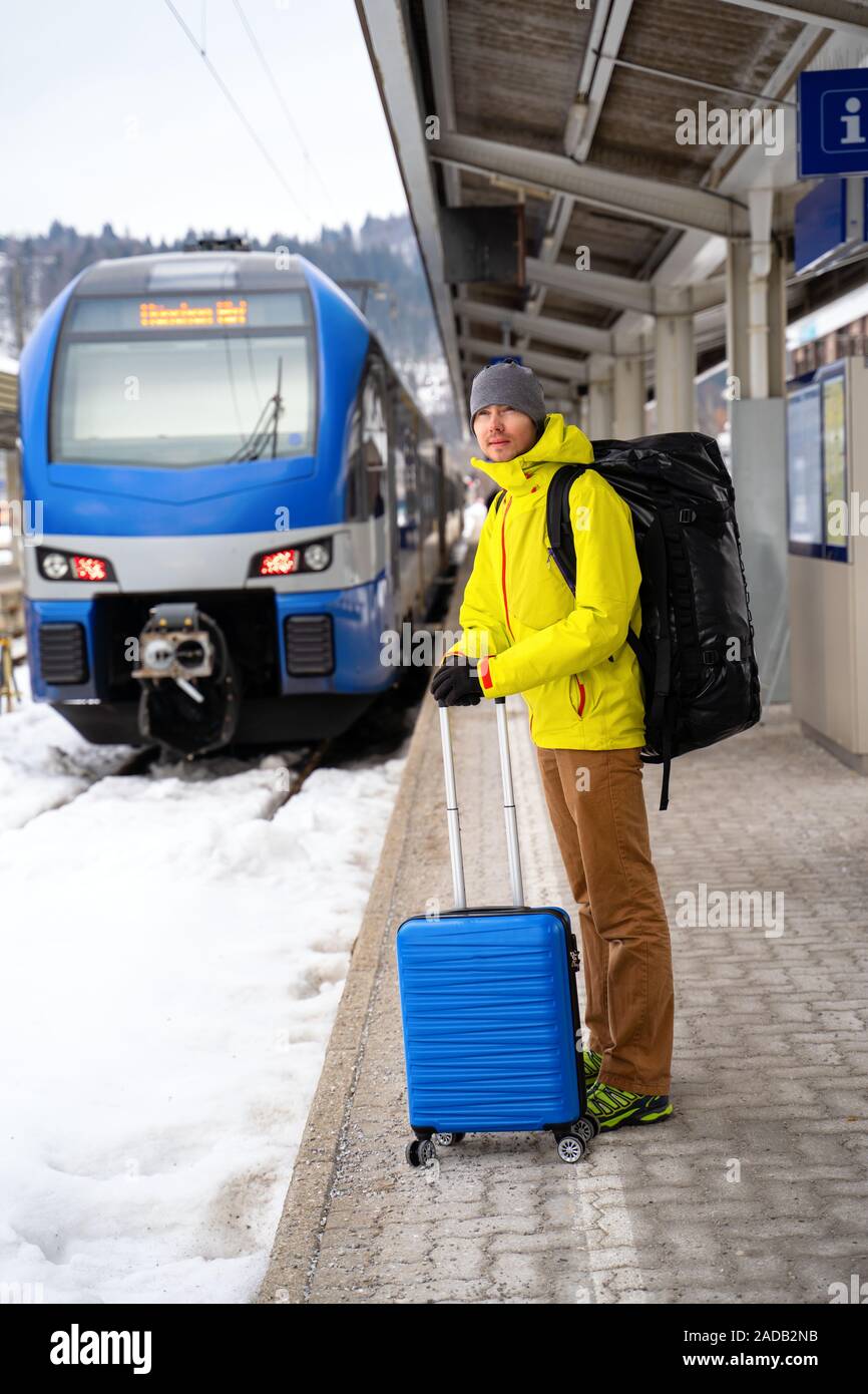 Per turisti in cerca di fotocamera con valigia blu alla stazione in attesa del treno contro sullo sfondo di montagne sulla giornata invernale Foto Stock