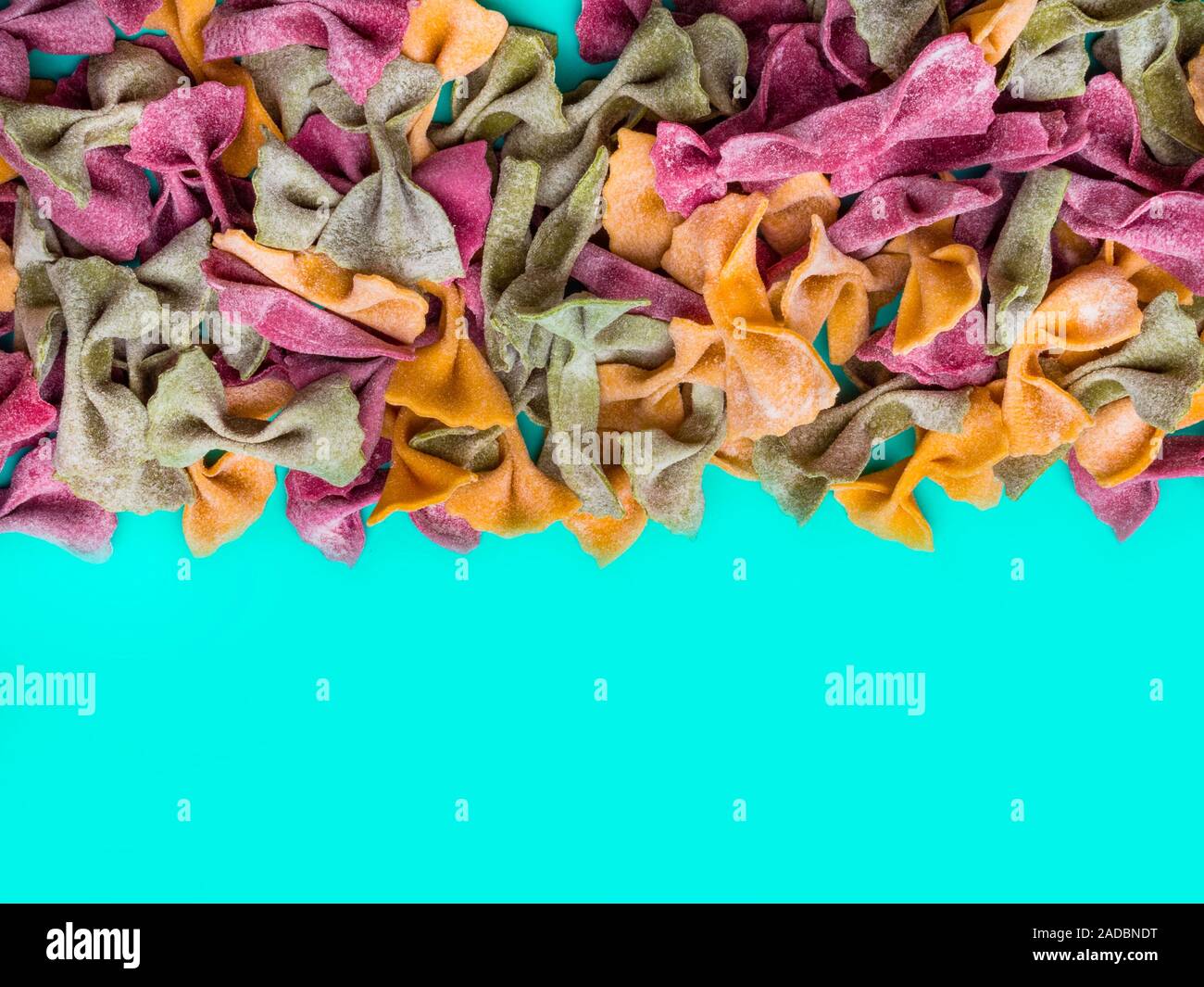 Pila di essiccato italiano Tricolore farfalle di pasta. Vari colori di bow tie blu su sfondo colorato Foto Stock