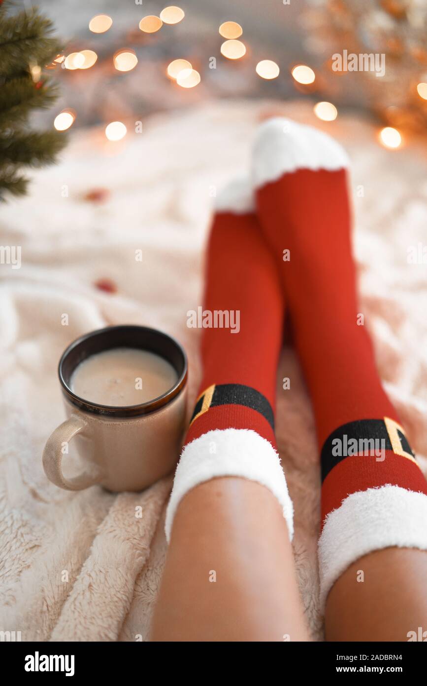 Lifestyle Home Foto di piedi in Santa calzini del vicino a un albero di Natale. Donna seduta presso la coperta, bevande bevande calde e rilassa il riscaldamento loro Foto Stock