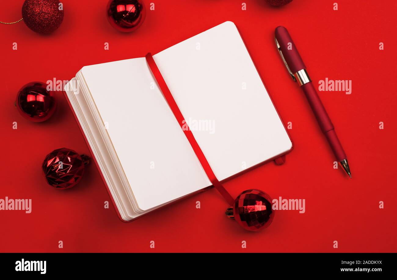 Rosso decorazioni di Natale, Notepad planner con penna su sfondo rosso. Copia dello spazio. Anno nuovo concetto di planata. Vista superiore laici piatta Foto Stock