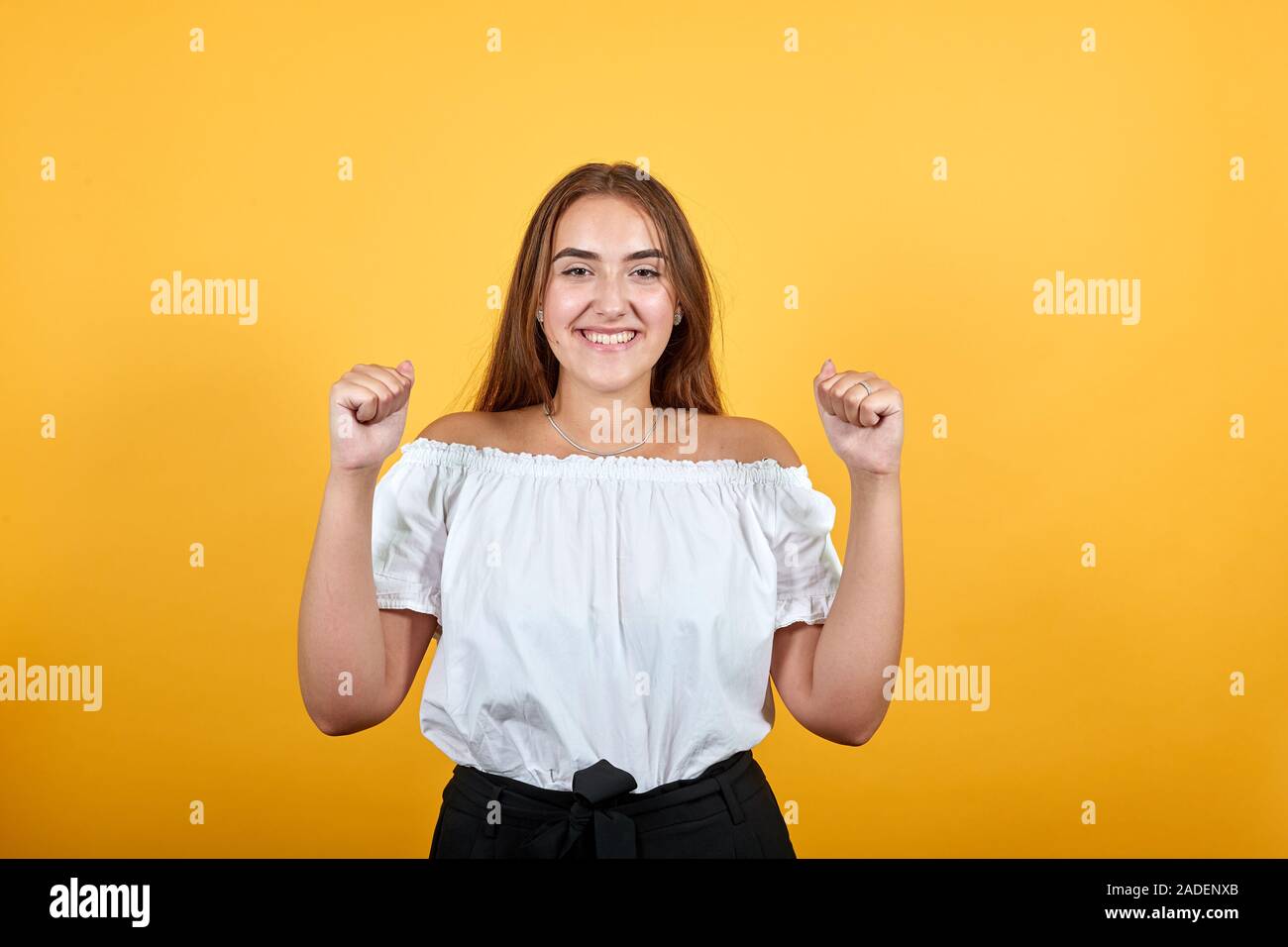 Felice giovane donna caucasica mantenendo i pugni fino, sorridente, cercando piuttosto Foto Stock